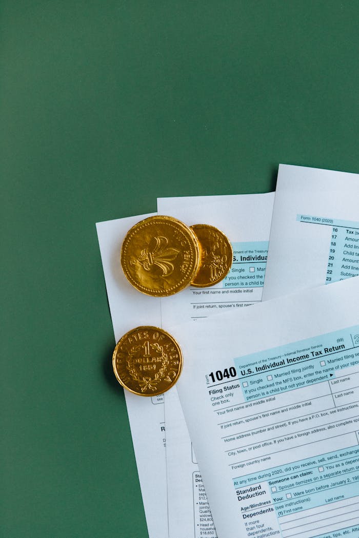 U.S. tax forms accompanied by gold coins, on a green surface, symbolizing finance.